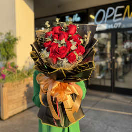 Bouquet of red roses wrapped in black paper with a gold ribbon
