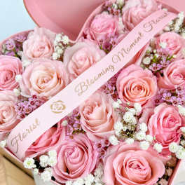 Pink roses arranged in a heart-shaped box with a ribbon
