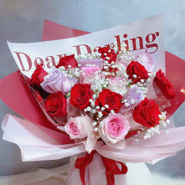 Bouquet of red, pink, and lavender roses with baby's breath in pink wrapping