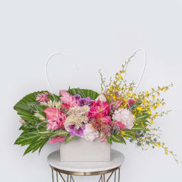 Wide tropical arrangement of pink, white, and yellow flowers in a low rectangular white container.