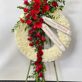 White funeral wreath with red roses and gerbera daisies on an easel