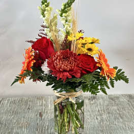 Mixed bouquet of red, orange, and yellow flowers in a glass jar vase