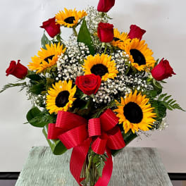 Bouquet of red roses and sunflowers with a red ribbon in a glass vase