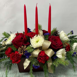 Holiday centerpiece with red candles, roses, and white blooms in a low container