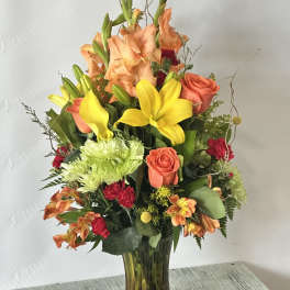Mixed bouquet of orange roses, yellow lilies, and green chrysanthemums in a glass vase