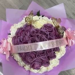 Purple and white rose bouquet with a pink anniversary ribbon and butterfly picks