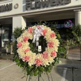 Pink and cream floral wreath on a stand with a white ribbon bow