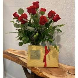 Red roses arranged in a vase with a gold Godiva gift box