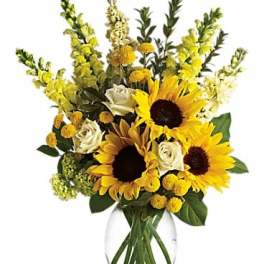 Bouquet of sunflowers, white roses, and yellow blooms in a clear glass vase