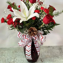 Red roses and white lilies arranged in a dark vase with a decorative bow.