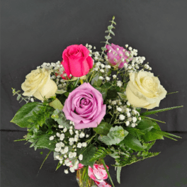 Small vase arrangement of cream, pink, and lavender roses with white filler flowers.