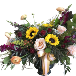Mixed bouquet with sunflowers, roses, and purple blooms in a dark vase