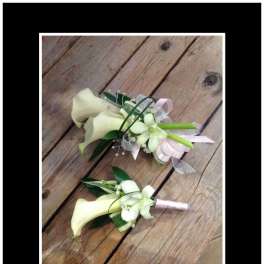 Two white calla lily boutonnieres with ribbon accents on wood