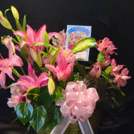 Pink lilies and alstroemeria in a basket with a pink ribbon bow