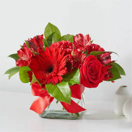 Red flowers arranged in a glass vase with a red ribbon