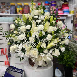 White floral arrangement in a wicker basket with a large satin bow