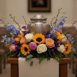Floral urn arrangement with sunflowers and roses around a silver urn