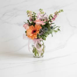 Pink and orange mixed bouquet in a clear glass vase with a ribbon