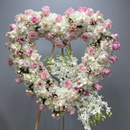 Heart-shaped floral wreath with pink and white roses and orchids on an easel