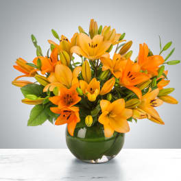 Orange lilies arranged in a round green glass vase