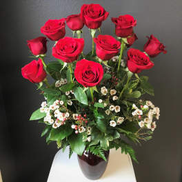 Red roses arranged in a dark vase with small white filler flowers