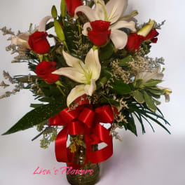 Bouquet of red roses and white lilies in a glass vase with a red ribbon