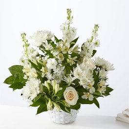 White floral arrangement in a white basket with a pale rose accent