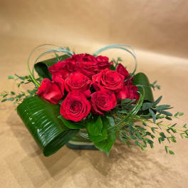 Red rose bouquet with decorative leaves in a low container