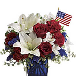 Red roses and white lilies in a blue glass vase with a small American flag