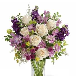 Bouquet of white roses and purple flowers in a clear glass vase