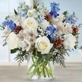 White roses and blue flowers arranged in a clear glass vase.