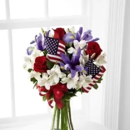 Bouquet of red, white, and purple flowers in a glass vase with small American flags