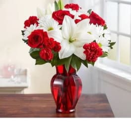 Red roses, white lilies, and white daisies in a red glass vase