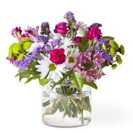 Mixed bouquet of daisies, carnations, and purple filler flowers in a glass vase