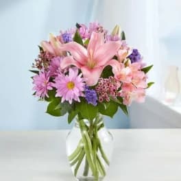 Pink lilies and purple daisies in a clear glass vase