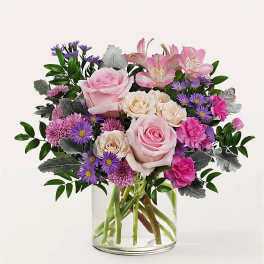 Pink and cream roses with purple flowers in a clear glass vase