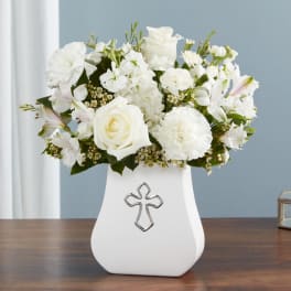 White floral arrangement in a white vase with a cross emblem
