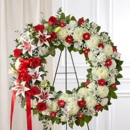 Red and white floral wreath on a black stand with a red ribbon