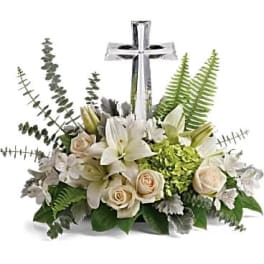 White lilies and cream roses arranged around a silver cross.