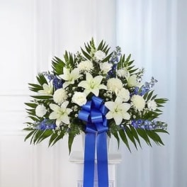 White floral standing spray with a blue ribbon on a pedestal