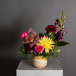 Mixed bouquet in a striped ceramic vase with pink, red, yellow, and purple blooms