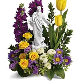 Floral arrangement with a white religious statue, yellow tulips, and purple flowers