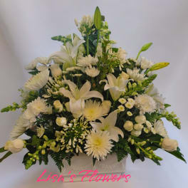 White floral arrangement in a rectangular vase with lilies and daisies