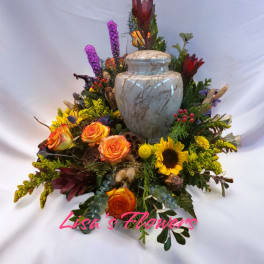 Mixed floral arrangement around a marble urn with orange roses and a sunflower