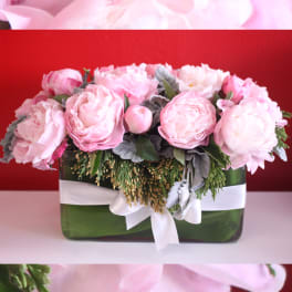 Pink peonies arranged in a green glass vase with a white ribbon