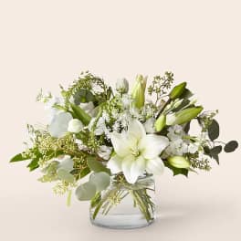 White lilies and mixed white flowers in a clear glass vase