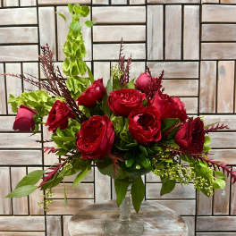 Red rose arrangement in a clear glass vase with green and burgundy foliage