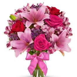 Pink lilies and roses in a glass vase with a pink ribbon