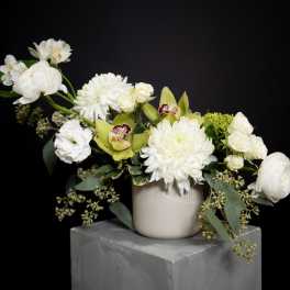 White floral arrangement in a beige vase with green orchids and roses