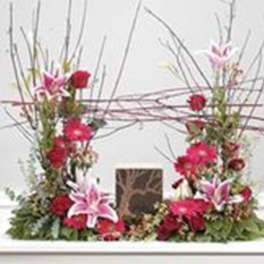 Tall floral arrangement with pink lilies and red flowers around a central vase